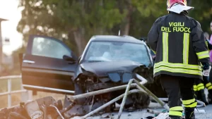 Firefighter at the scene of a car crash with damaged vehicle and debris.