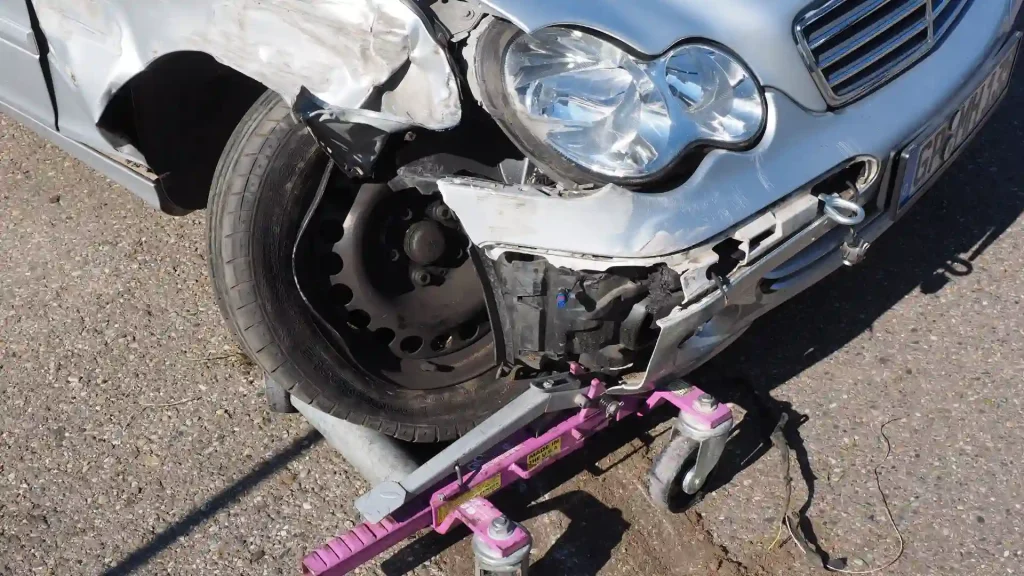 Close-up of a car with a damaged front bumper and wheel, mounted on a repair dolly.