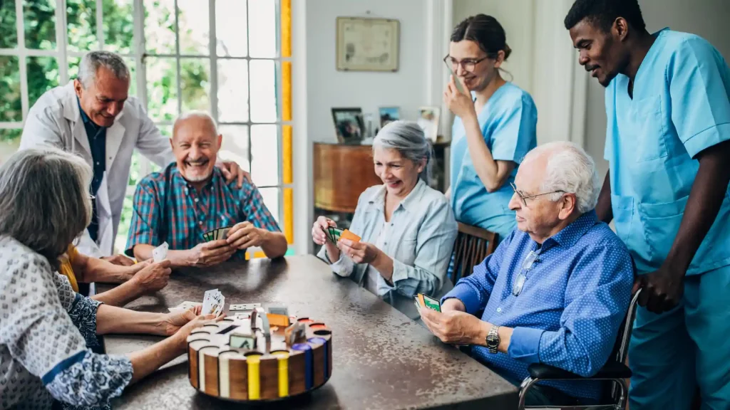 Elderly residents playing cards with caregivers in a common room